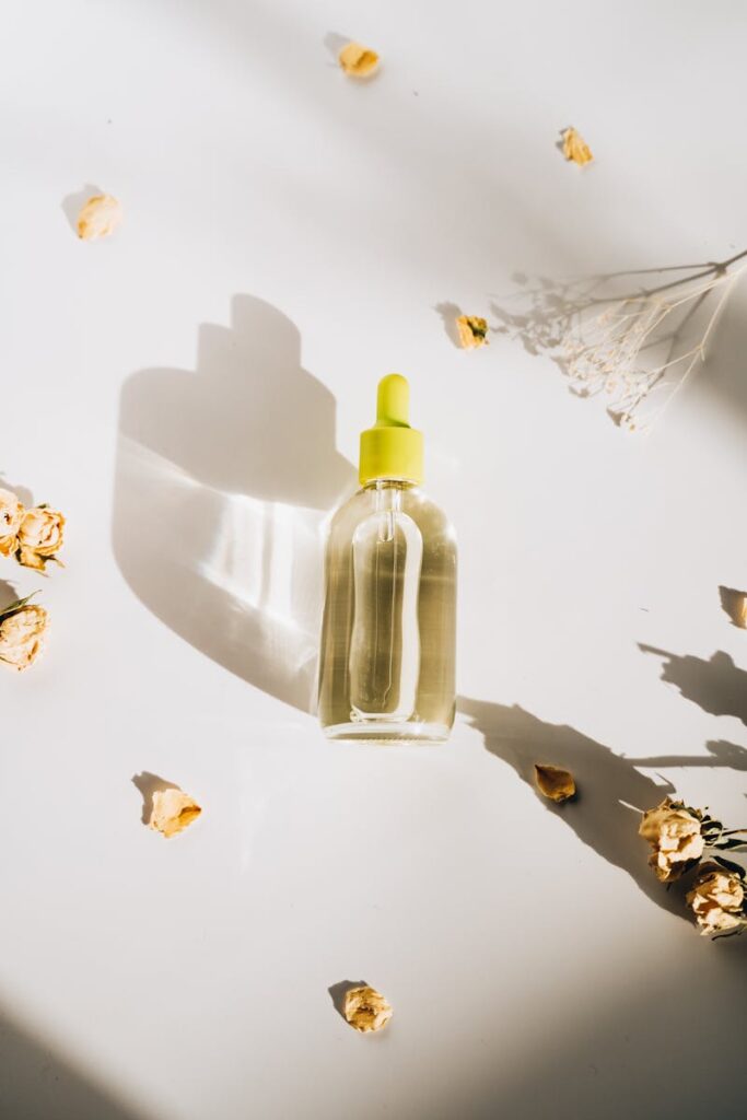 Elegant still life of a serum bottle surrounded by dried flowers, casting a soft shadow.