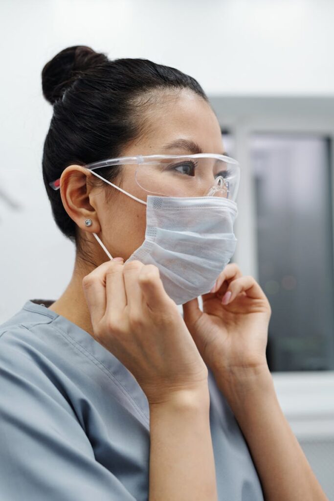 Asian female healthcare worker putting on a protective mask indoors, emphasizing health and safety.